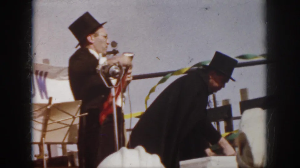 1958 Virginia 8mm still of a top-hatted magician holding a red handkerchief near a microphone during an outdoor stage act.