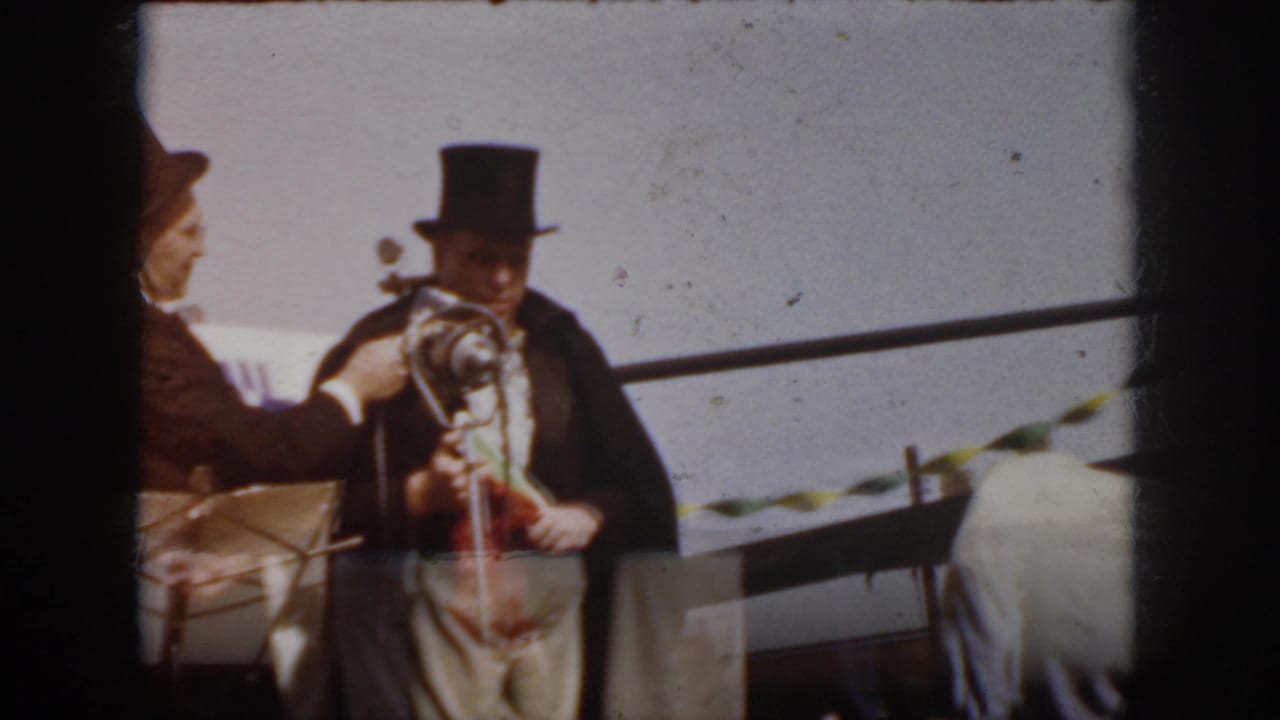 1958 Virginia frame with a woman beside a man in a top hat at a microphone during an outdoor public gathering.