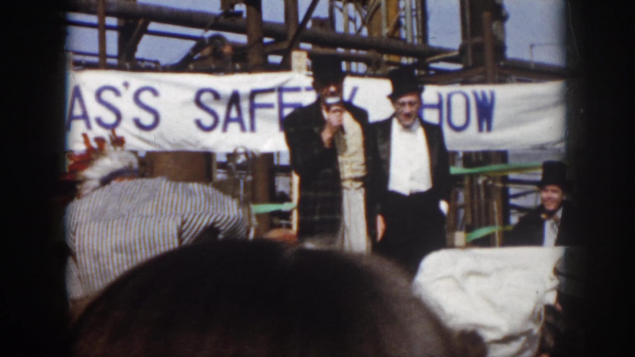1958 Virginia 8mm frame showing two formally dressed men on an outdoor industrial stage beneath a SAFETY SHOW banner.
