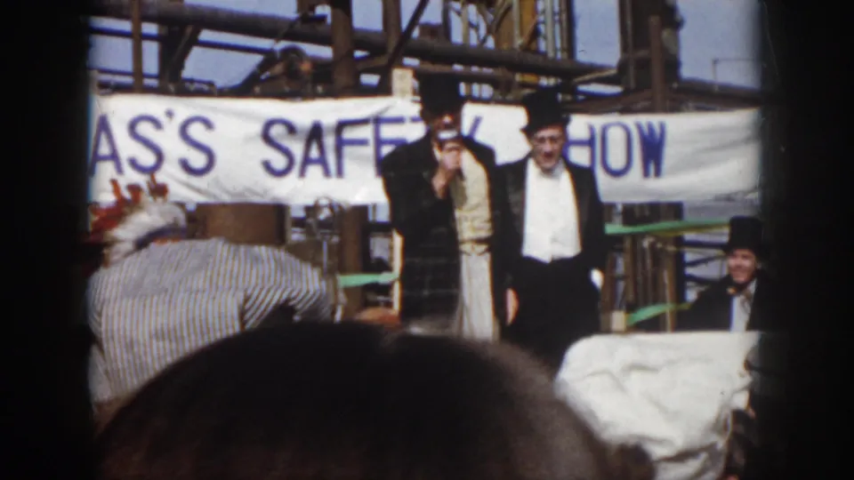 1958 Virginia 8mm frame showing two formally dressed men on an outdoor industrial stage beneath a SAFETY SHOW banner.