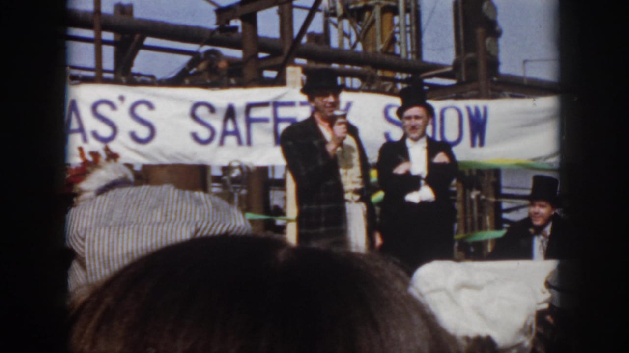 A top-hatted man speaks into a microphone while another man stands beside him near the banner.