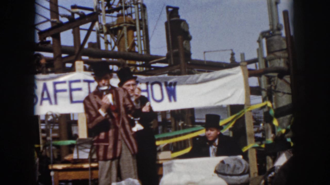 Virginia 1958 frame of a top-hatted presenter speaking into a microphone, with another costumed man and industrial structures behind him.