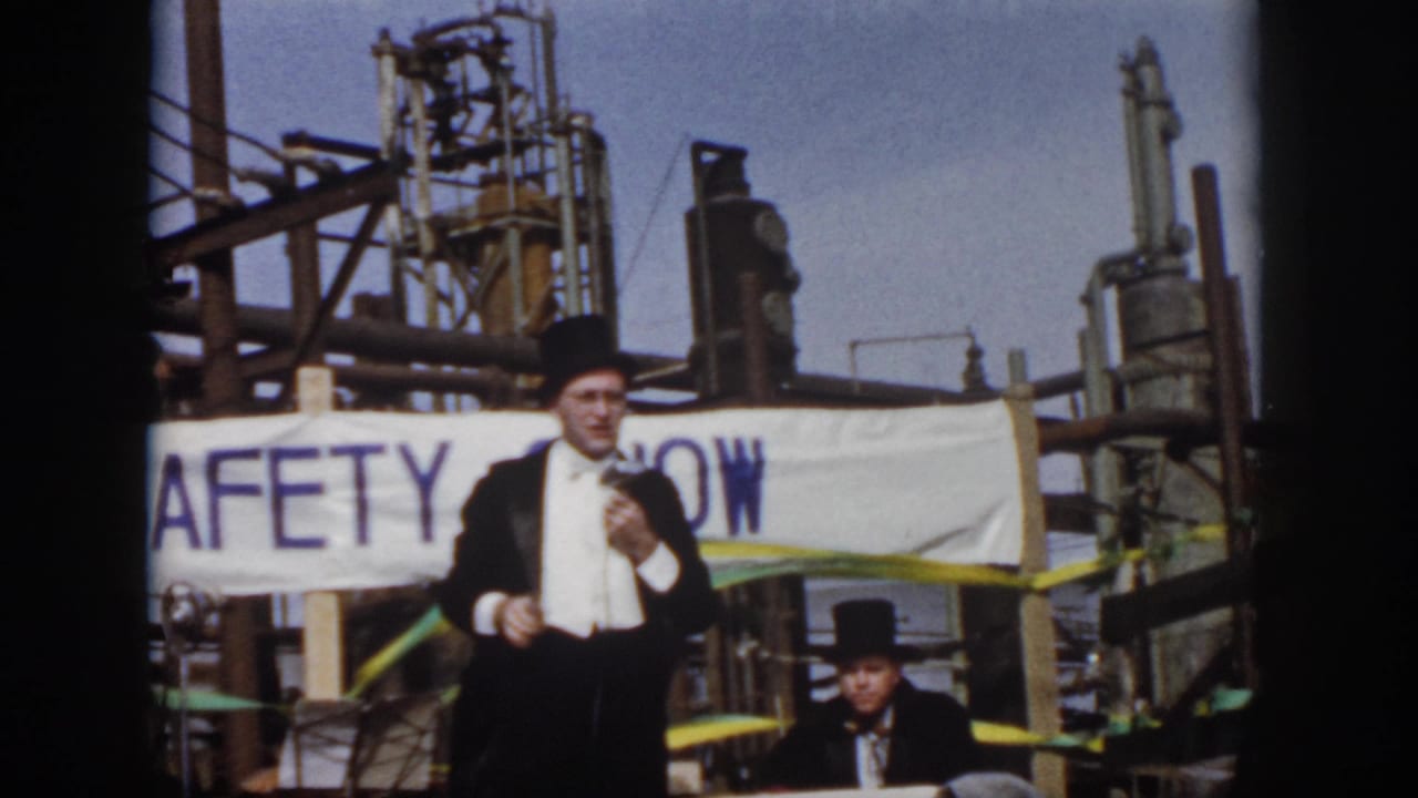 1958 Virginia safety show frame with a formal-costumed speaker, seated man, banner, colored streamers, and industrial equipment behind them.