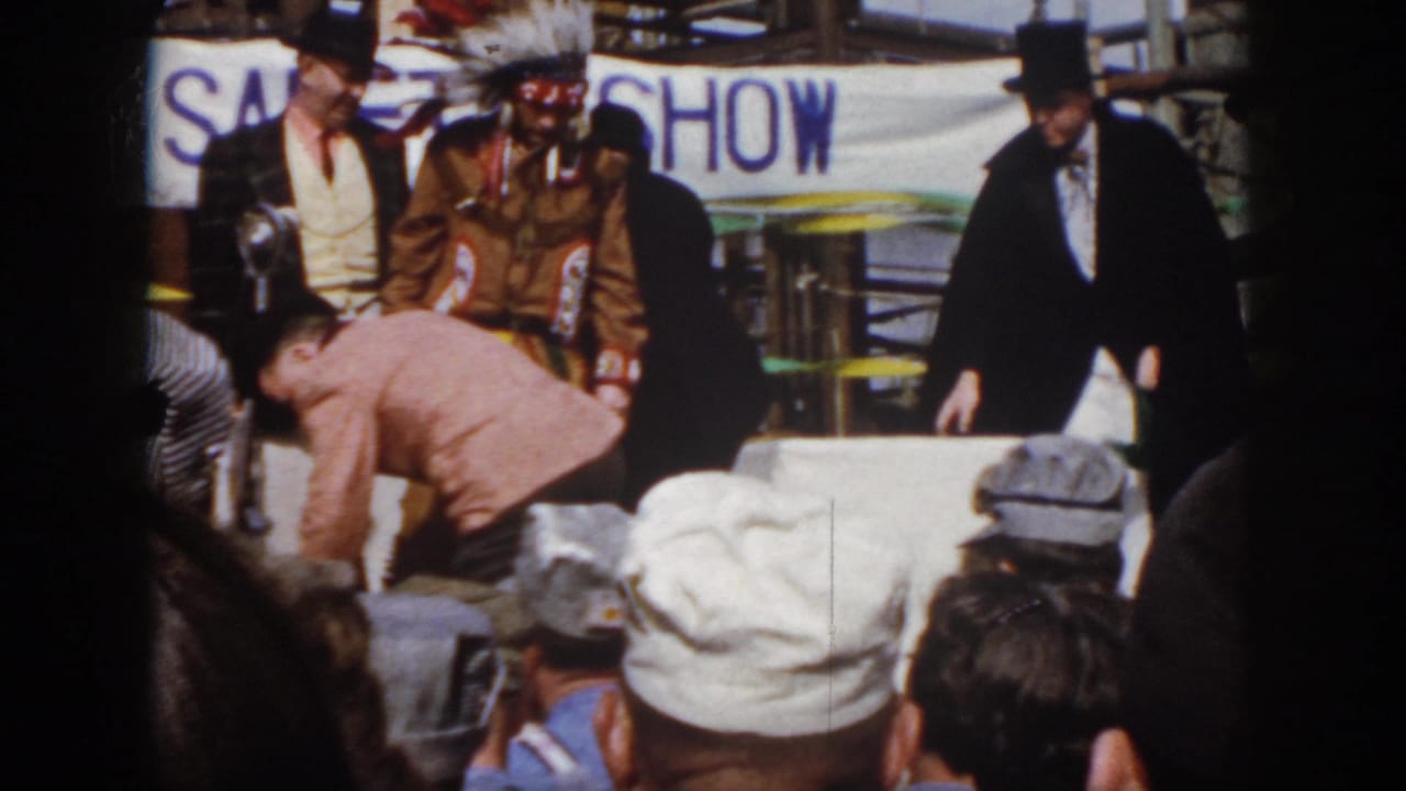 1958 Virginia safety-show scene with a man in Native American regalia, a tuxedoed figure, audience members, and industrial backdrop.