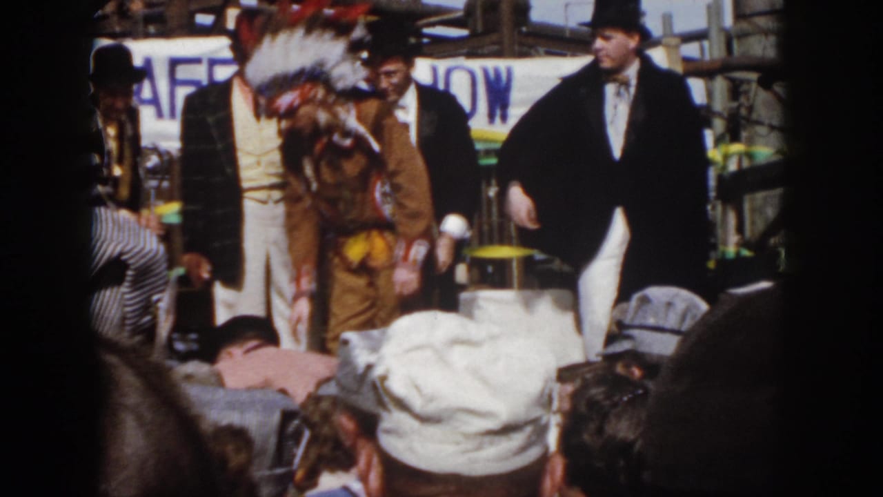1958 Virginia frame showing a costumed safety-show performer in Native American regalia beside tuxedoed men and seated spectators.