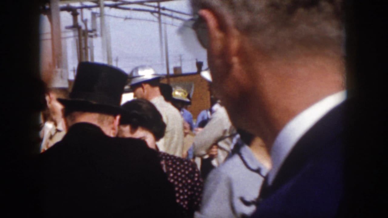 1958 Virginia event frame from behind the audience, showing the magician's top hat, nearby spectators, and uniformed or work-clothed people near the stage area.