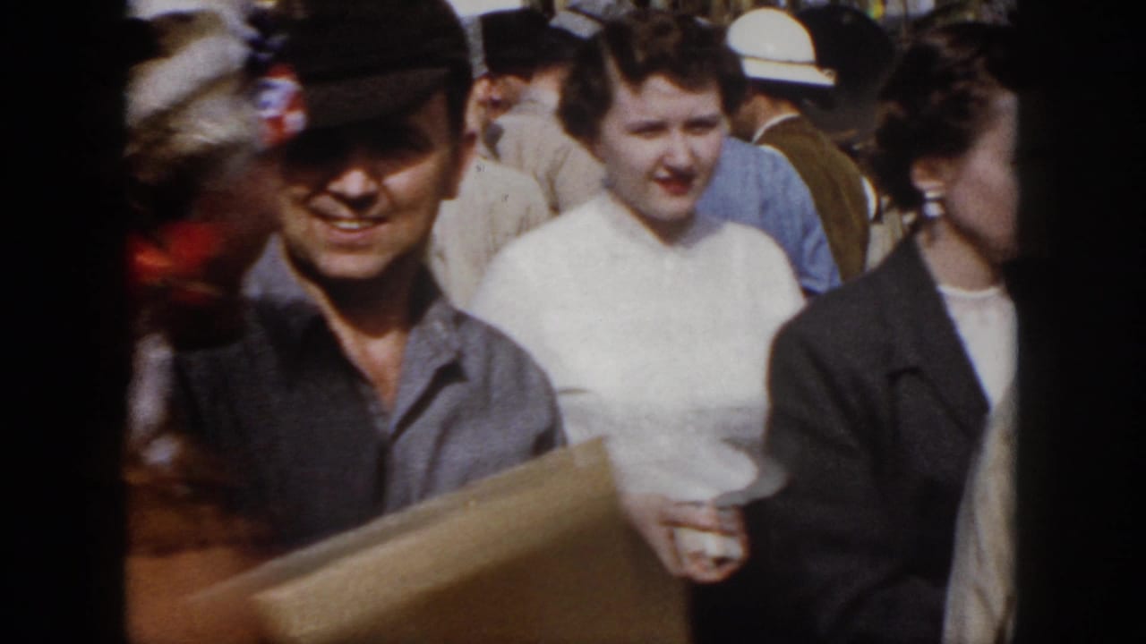 1958 Virginia home-movie frame showing smiling adults in a crowded outdoor event, with a man in a dark cap near the center.