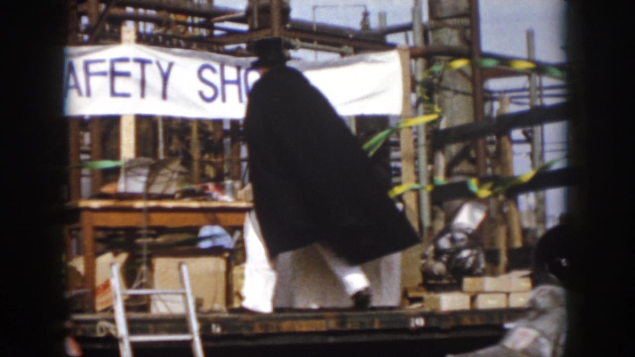 In Virginia 1958 home-movie footage, a caped figure stands on a fair platform under a SAFETY SHOW banner amid industrial structures.