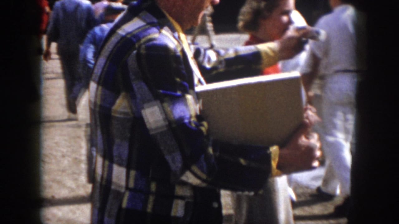 A man in a blue plaid shirt holds a folder while standing among attendees at the 1958 Virginia industrial fair.