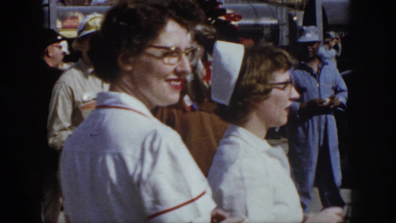 1958 Virginia home-movie still of a smiling nurse with glasses beside another uniformed woman at an outdoor gathering.