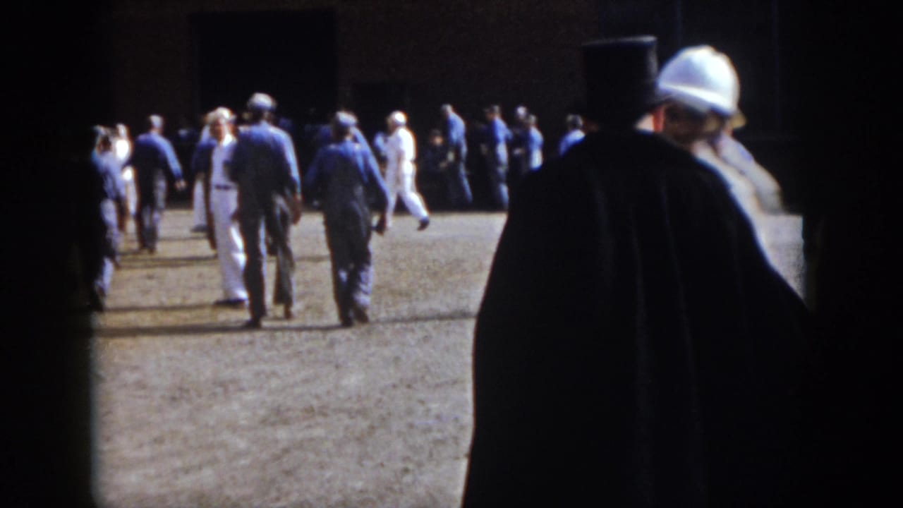 1958 Virginia home-movie frame showing men walking and milling outdoors, with dark foreground obstruction and bright pavement.