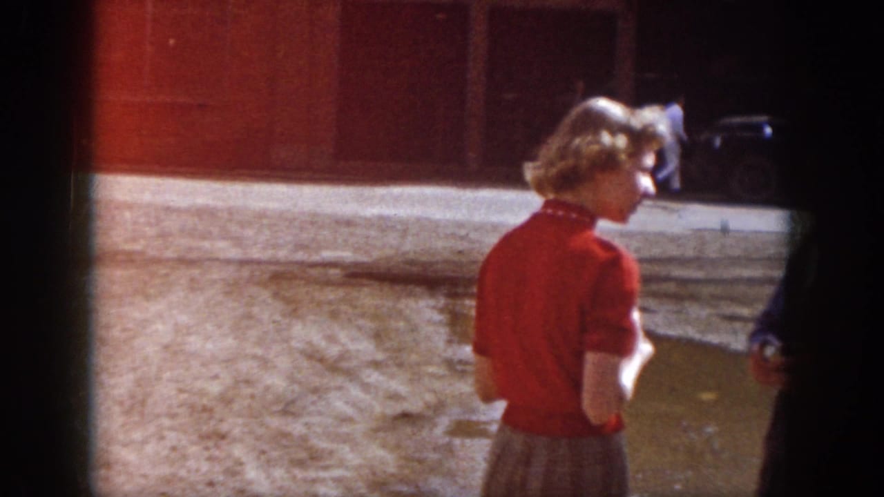 1958 Virginia frame with a woman in a red blouse and skirt standing near a muddy lot and building frontage.