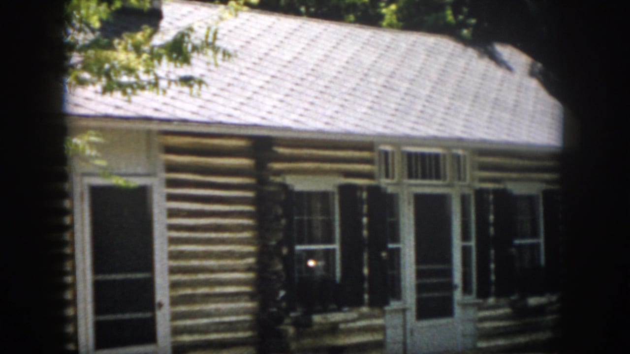 1958 Virginia cabin exterior with a screened front door, white framing, dark shutters and horizontal log walls.