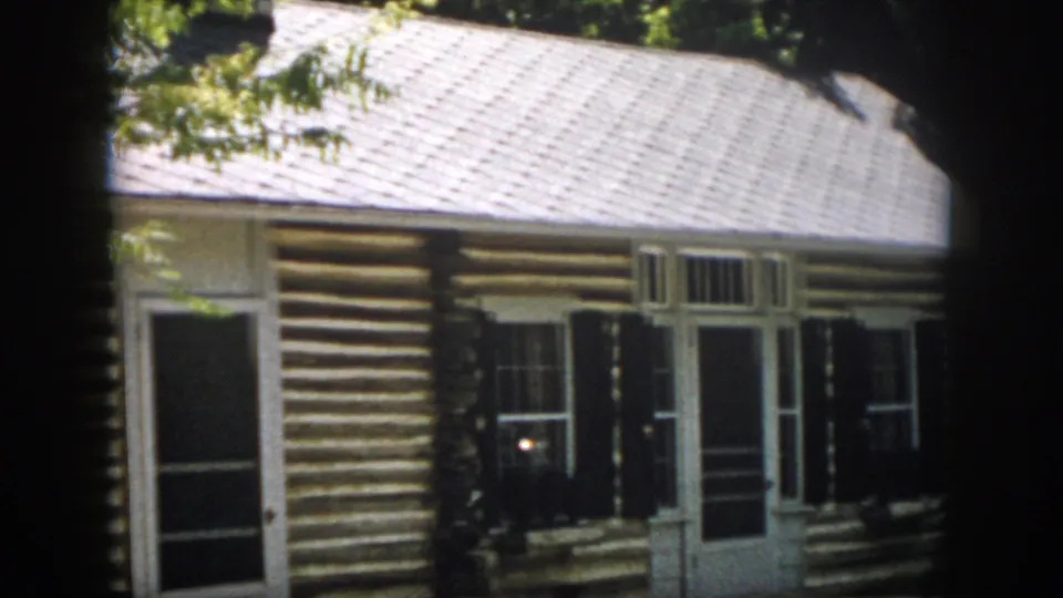 1958 Virginia cabin exterior with a screened front door, white framing, dark shutters and horizontal log walls.