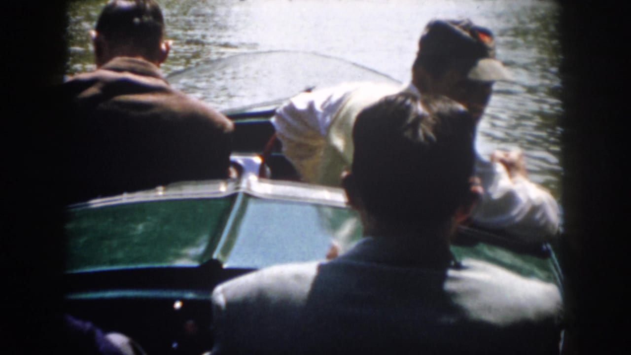 Rear view of several adult men aboard a green motorboat on a river in supported 1958 Virginia home-movie footage.