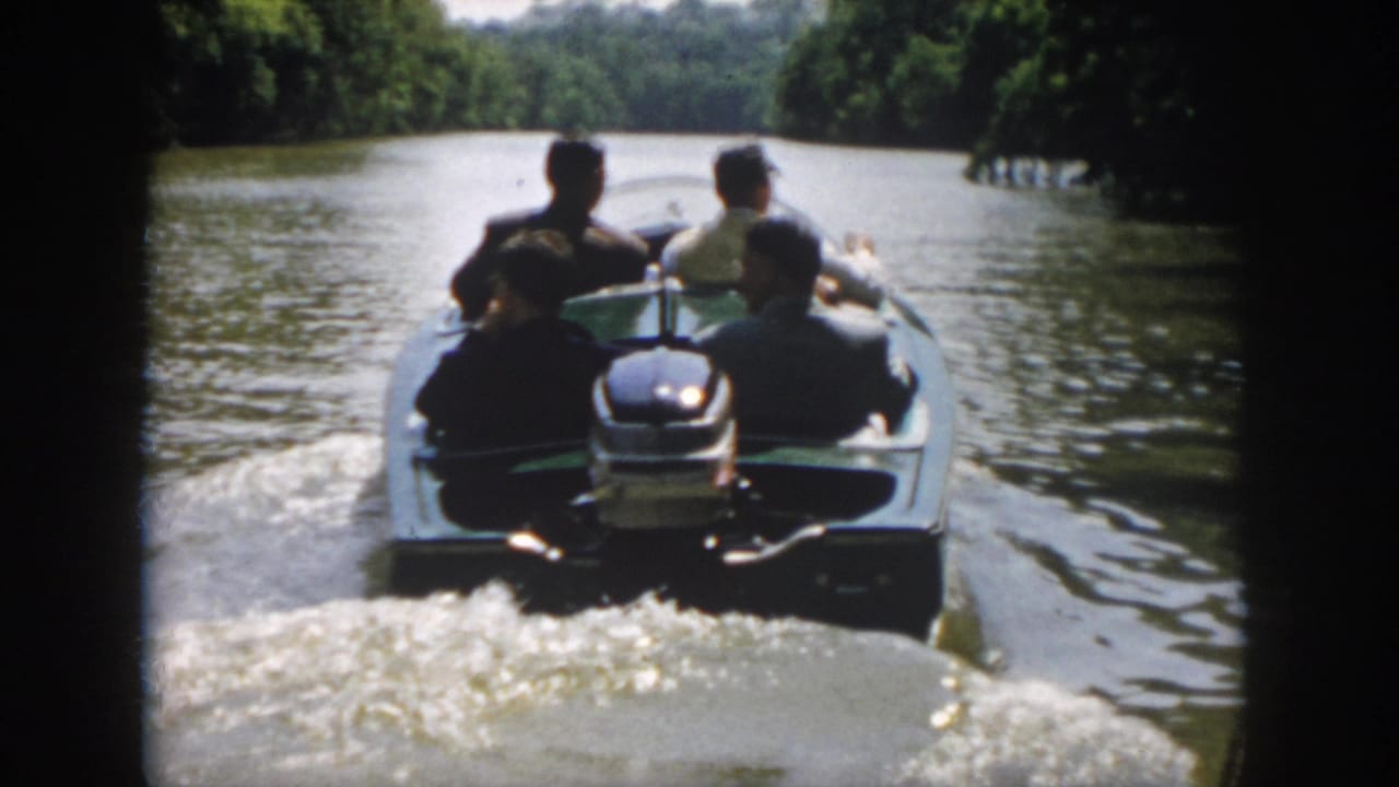 1958 Virginia 8mm frame showing four adult men in an open motorboat moving away along a tree-lined river.