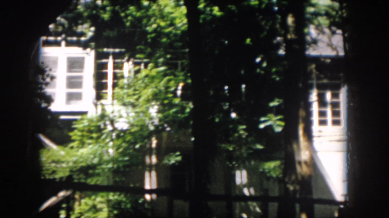 Final 8mm frame of the Virginia building partly screened by trees, with white windows and foliage in strong sunlight.
