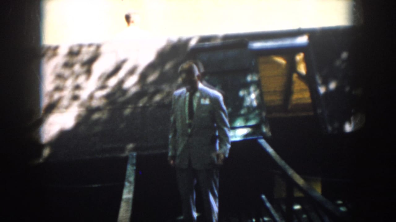 A man in a light suit and tie walks down exterior stairs outside a Virginia residence in 1958 home-movie footage.