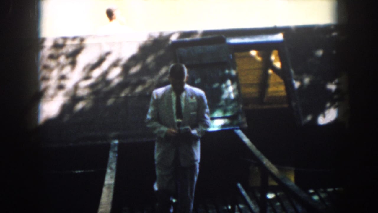 In 1958 Virginia home-movie footage, a suited man moves down a shaded wooden stair or ramp toward the camera.