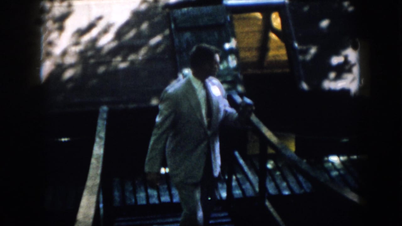 Suited man walks along the railing in a dark, shadowed exterior passage.