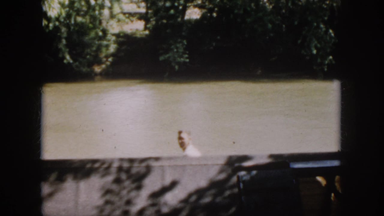 A distant waterside figure in a light top appears below trees, framed by dark interior edges in the 1958 Virginia footage.