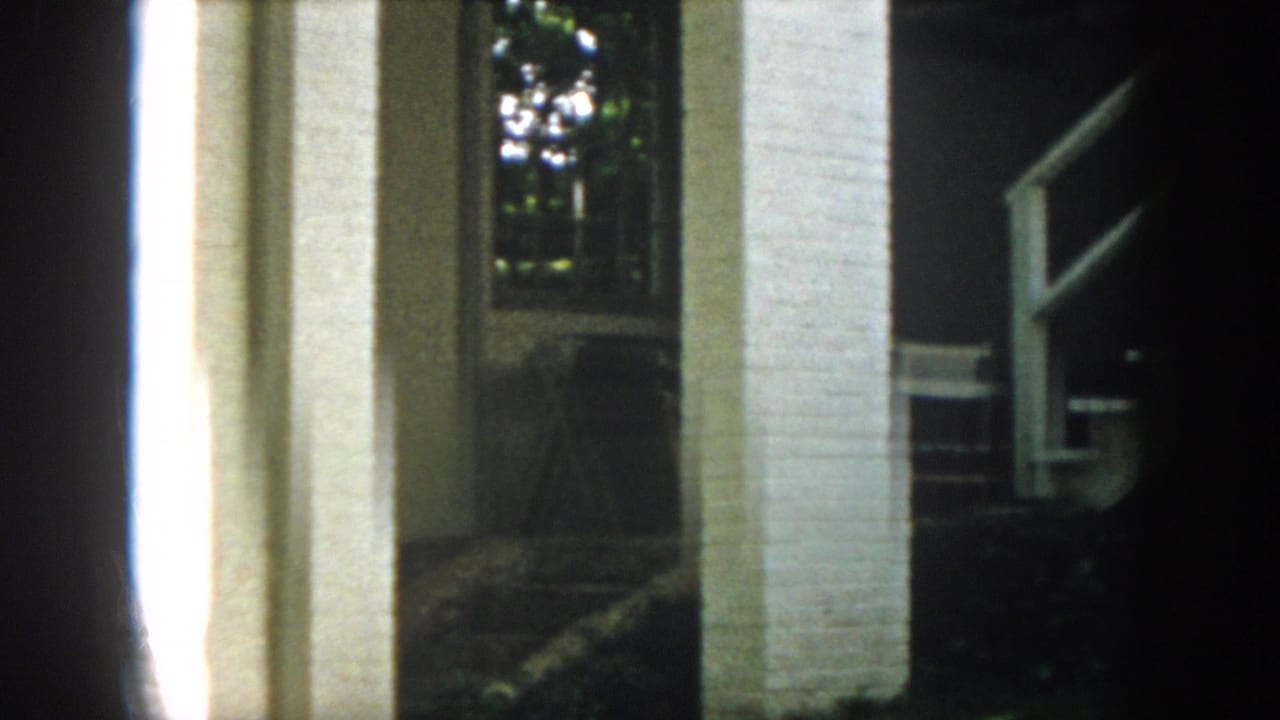 1958 Virginia 8mm frame showing white brick porch columns, a dark entry area, and leafy trees in the background.