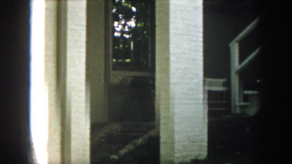 1958 Virginia 8mm frame showing white brick porch columns, a dark entry area, and leafy trees in the background.