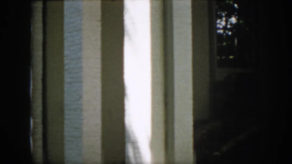 Virginia home-movie frame from 1958 with white brick columns, a shaded porch opening, and faint window detail near trees.