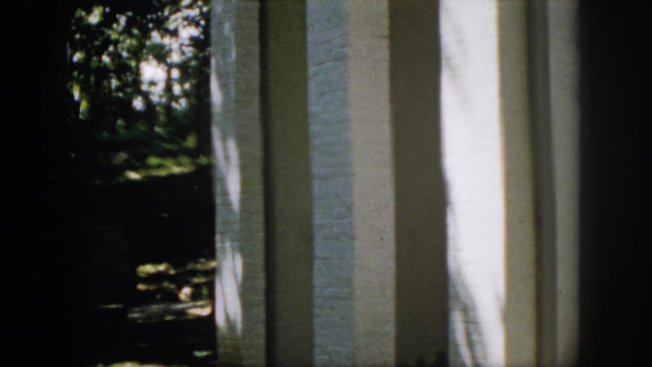 1958 Virginia 8mm view of a white brick wall or column with a dark wooded yard visible to the side.