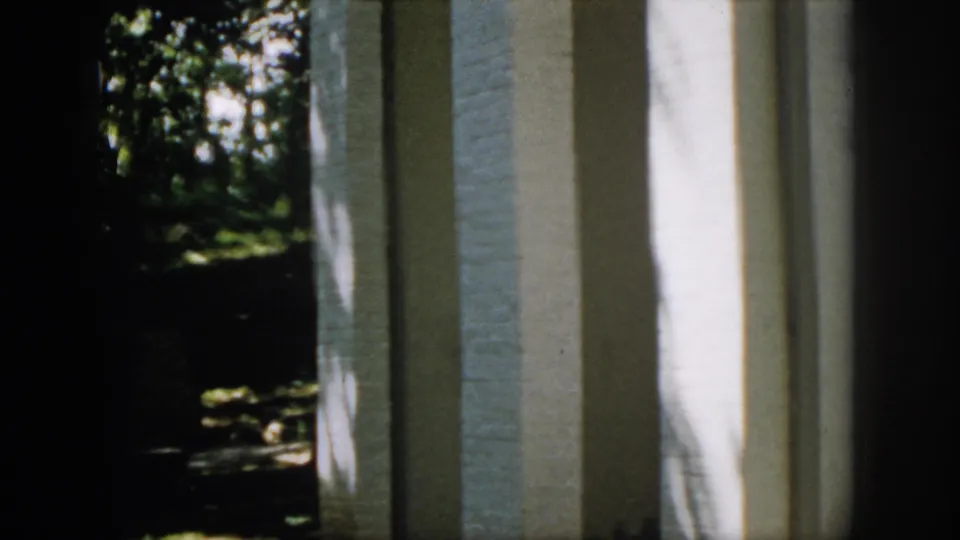 1958 Virginia 8mm view of a white brick wall or column with a dark wooded yard visible to the side.