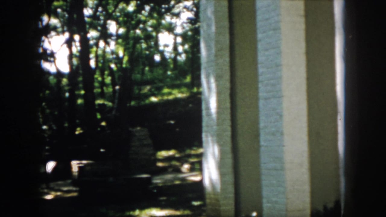 Final 1958 Virginia frame showing porch columns beside a shaded yard, trees, and possible low masonry or steps.