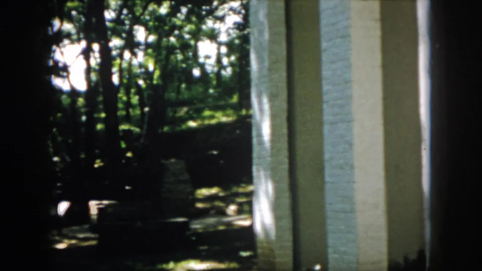 Final 1958 Virginia frame showing porch columns beside a shaded yard, trees, and possible low masonry or steps.