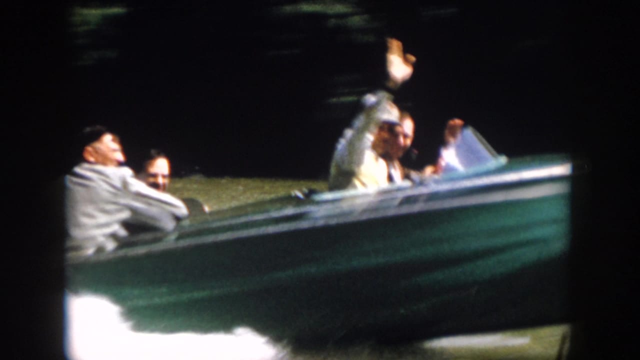 Close 1958 Virginia home-movie view of adults riding in a green motorboat, including a man raising his hand toward the camera.