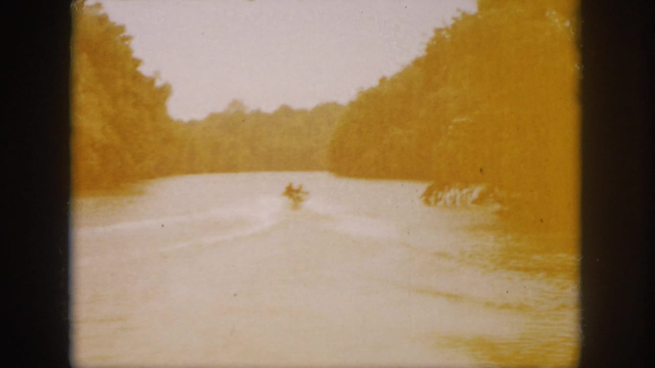 1958 Virginia 8mm frame showing the boat far down a broad wooded river, with warm exposure and visible film edges.