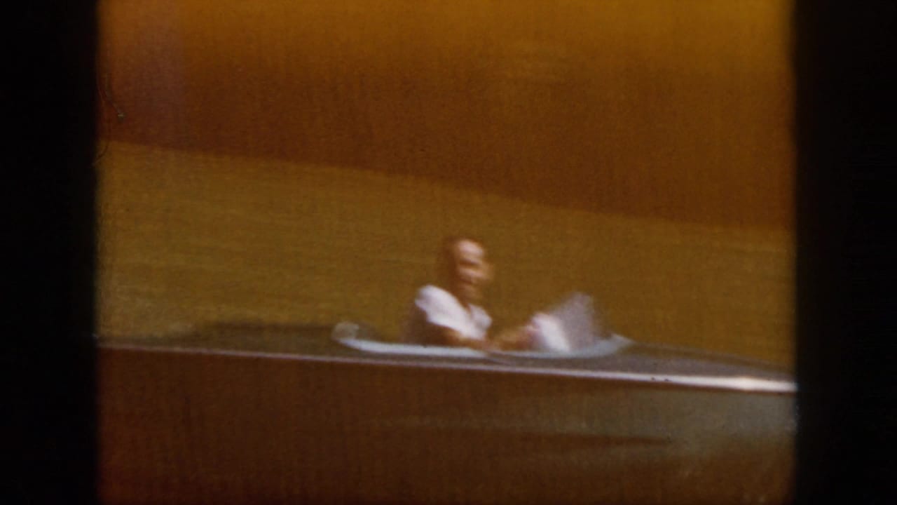 1958 Virginia river scene with a person seated at the helm of a small motorboat, framed softly on faded 8mm film.