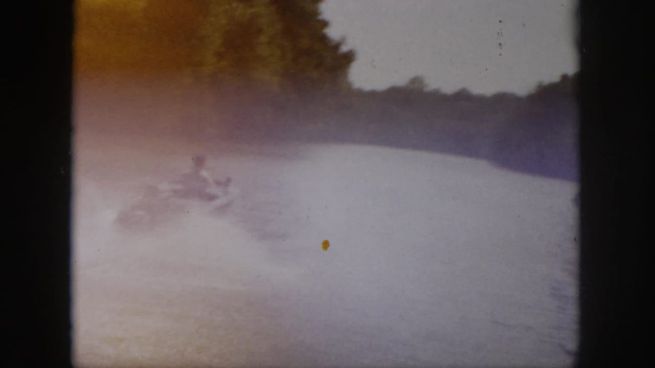 Faded 1958 Virginia 8mm frame showing a motorboat speeding through river spray near a wooded shoreline.