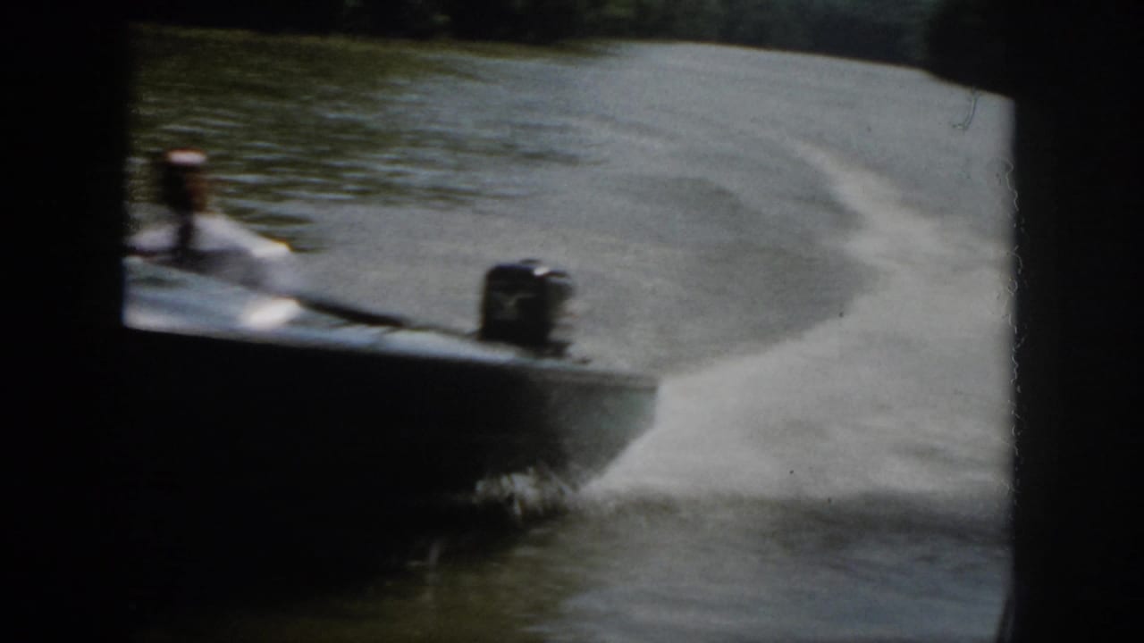 Close 1958 Virginia home-movie view of a motorboat rushing past, with blurred hull, outboard motor, spray, and river wake.