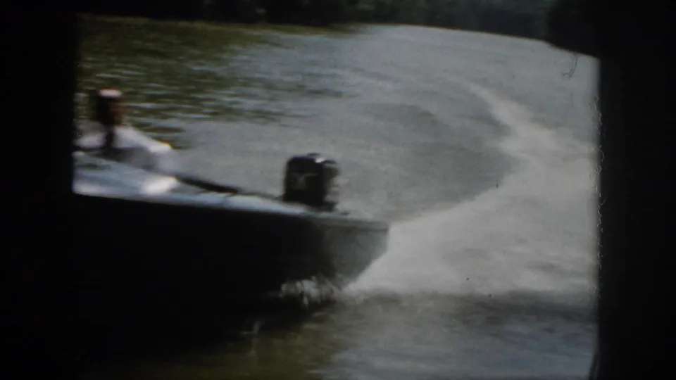 Close 1958 Virginia home-movie view of a motorboat rushing past, with blurred hull, outboard motor, spray, and river wake.