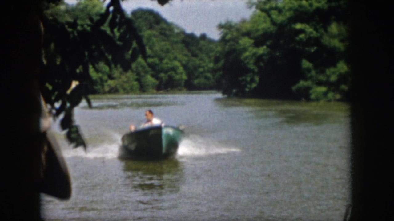 1958 Virginia home-movie frame showing a small motorboat speeding toward the camera on a tree-lined river with wake on both sides.