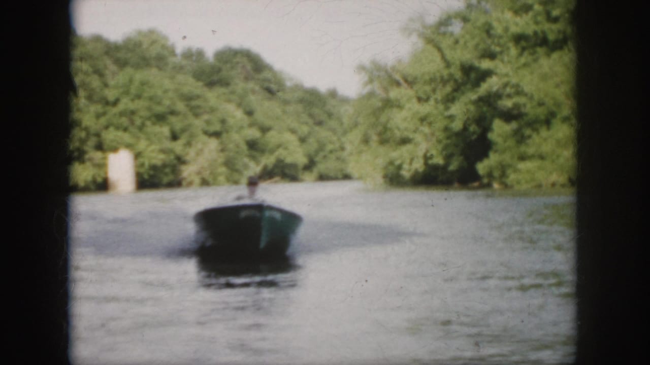 Motorboat seen farther away on the river with trees along both banks.