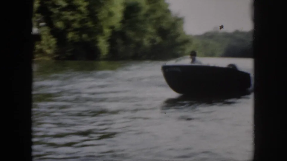 The boat comes toward the camera on a wooded Virginia river, with the driver faintly visible against soft 8mm exposure.
