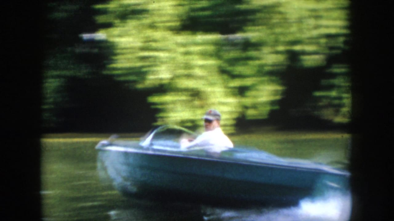 A capped adult driver passes close by in a small blue motorboat, creating spray on the Virginia river in 1958 8mm footage.