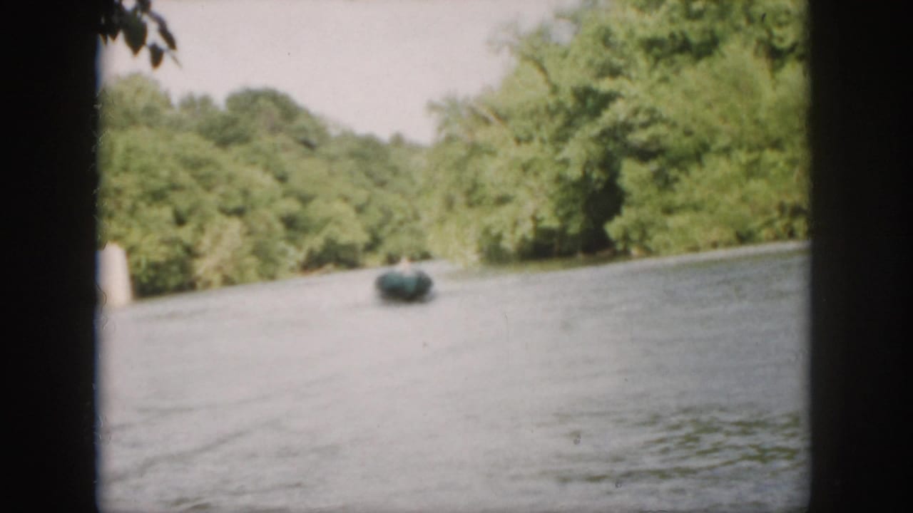 1958 Virginia 8mm frame showing a small green motorboat moving across a calm wooded river at a distance.
