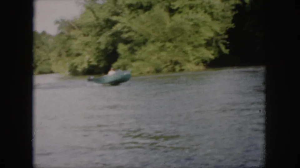 A green motorboat passes along a wooded Virginia river in soft 1958 8mm home-movie footage.