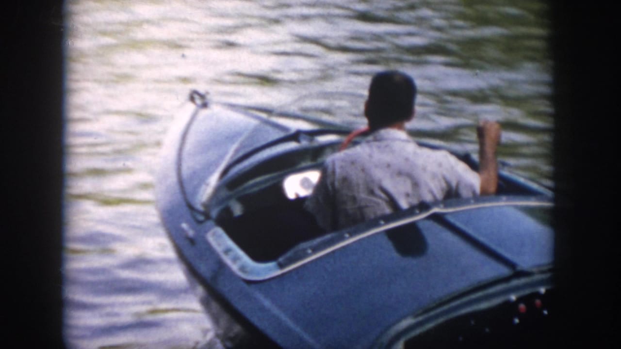 Rear view of a man seated in a green speedboat moving across lake water.