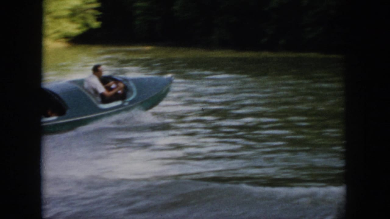 Wide 1958 Virginia home-movie view of the green speedboat moving across the lake with a wooded shoreline beyond.