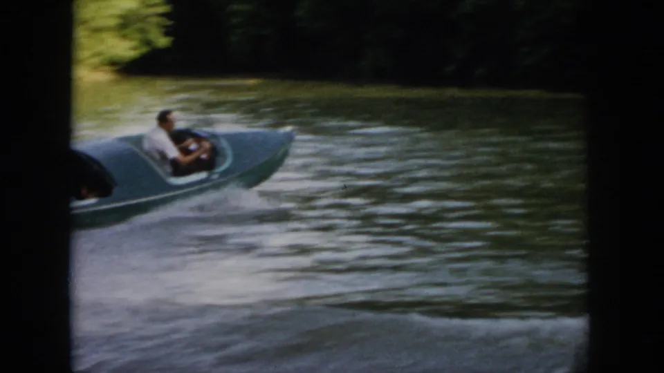 Wide 1958 Virginia home-movie view of the green speedboat moving across the lake with a wooded shoreline beyond.