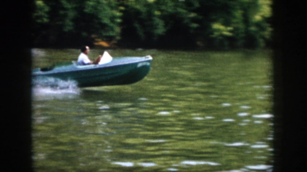 Small blue motorboat with a man aboard moves across green river water.