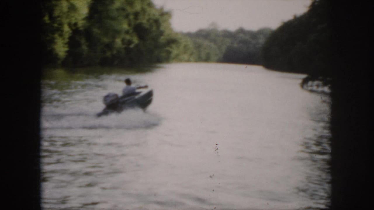 Wide 1958 Virginia home-movie view of a small motorboat turning on a broad river with trees on both banks.
