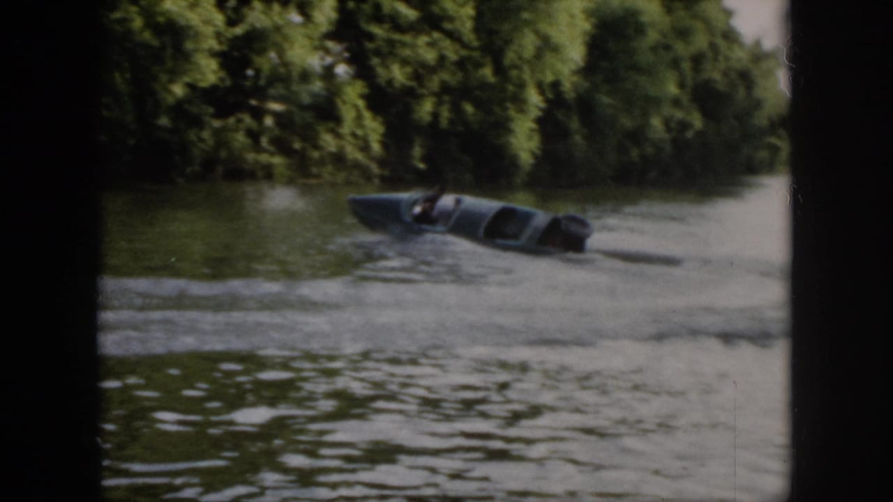 1958 Virginia frame of a small blue motorboat leaning into a circular turn on a wooded river.